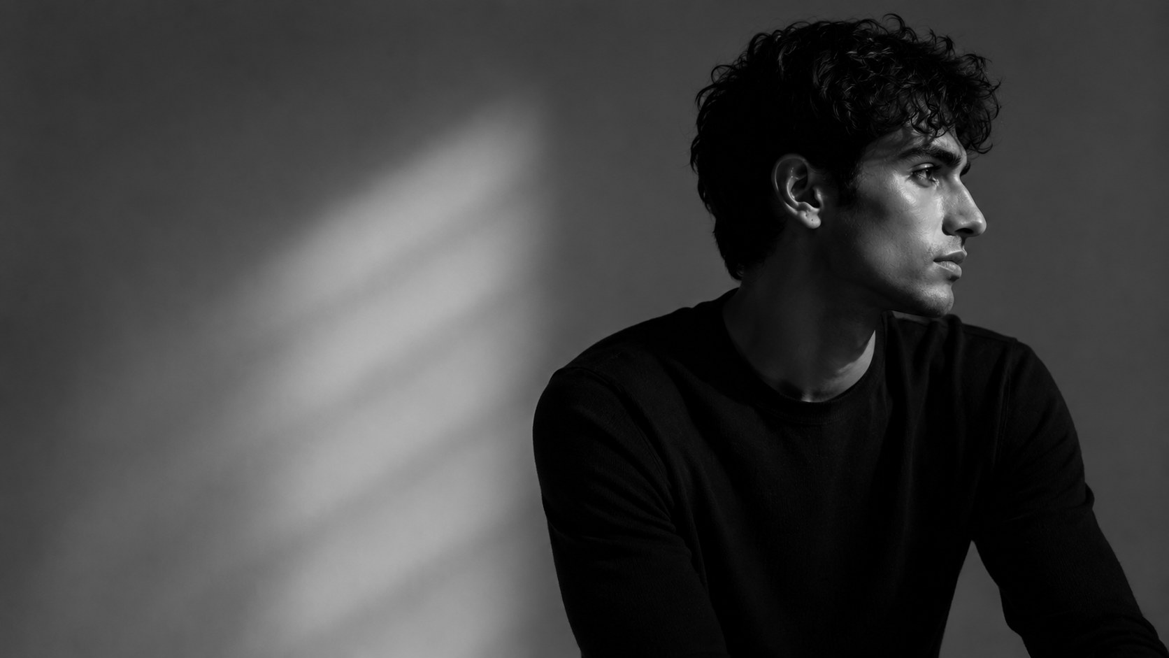 A creator in a black sweater looks out of frame, photographed in black and white
